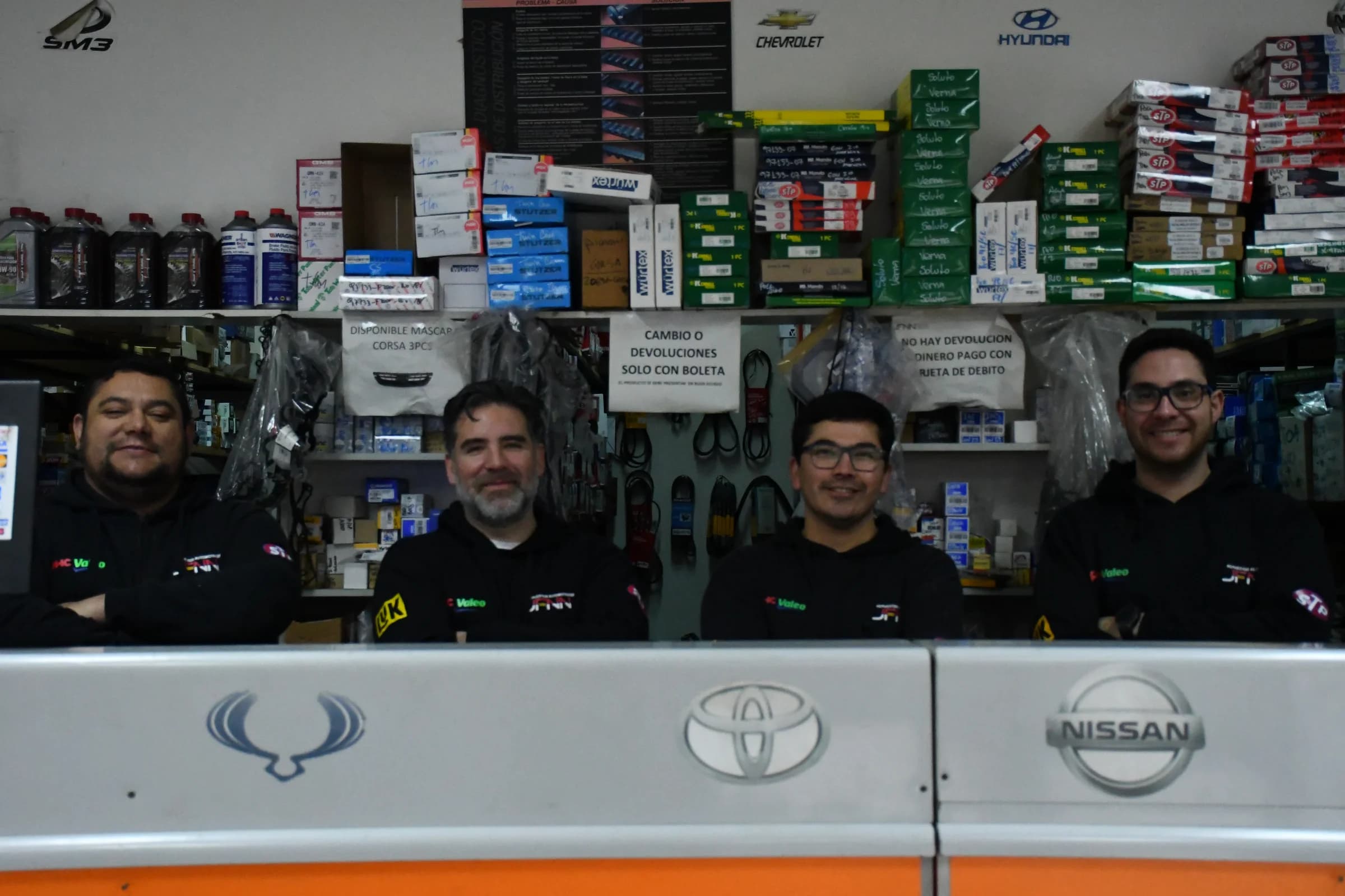 Los cuatro integrantes del equipo de Repuestos Automotrices JFNN en el mostrador del local de Melipilla, rodeados de repuestos en sus estantes